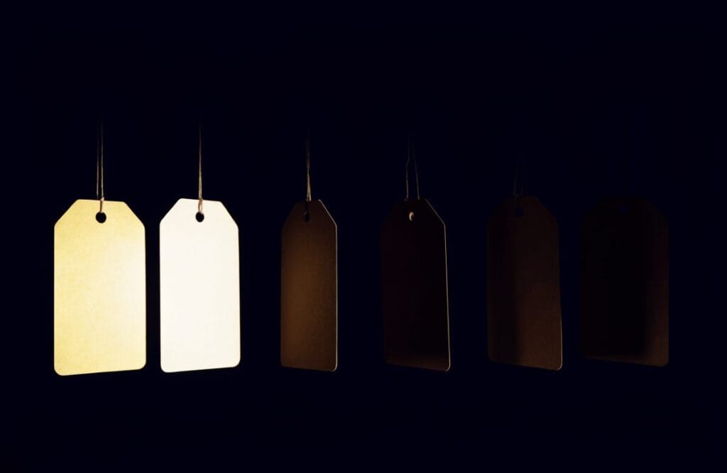 Six blank price tags in a row with only two lit and four receding into darkness, illustrating that only two of six CLAT institutes publish a real programme fee.