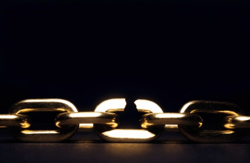 A chain of heavy brass links lit against darkness with the centre link snapped open, representing the broken step in an argument that CLAT logical reasoning questions ask you to find.