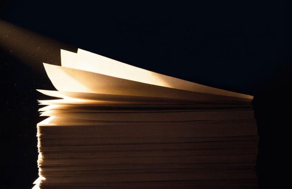 A deep stack of past exam papers fading into shadow with only the top three sheets lifted and lit, illustrating that just three CLAT past papers match the current format.