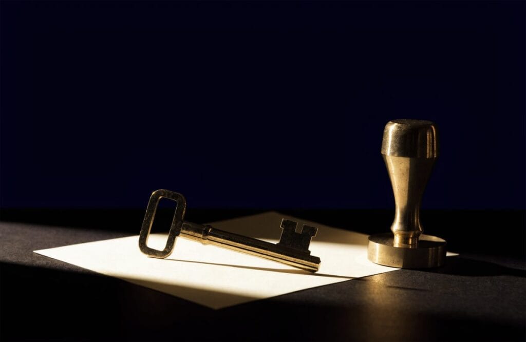 A brass key lying across a blank application form beside a brass rubber stamp, representing that a CLAT score opens NMIMS admission only after you complete a separate NMIMS registration.